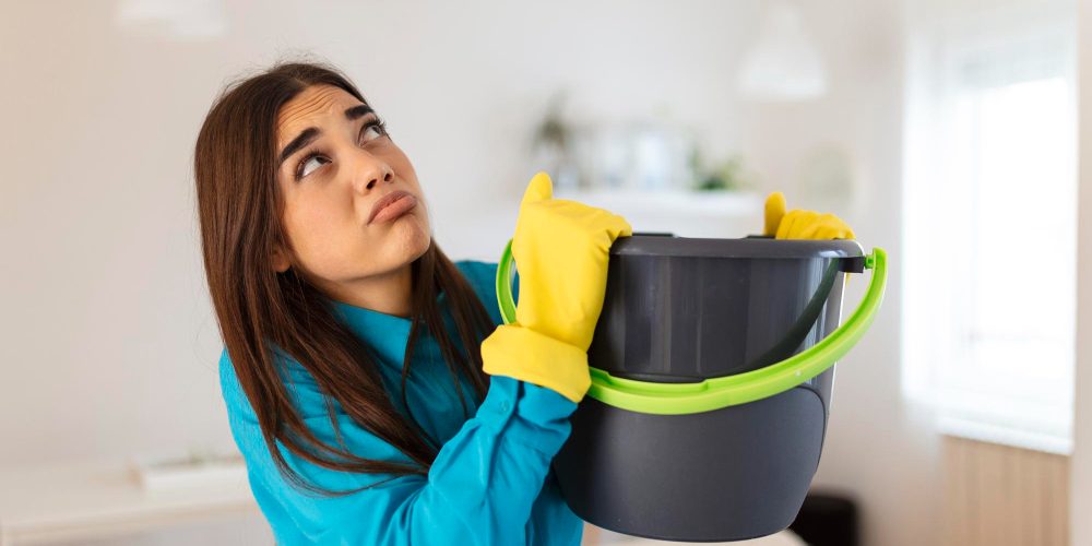 shocked-woman-looks-ceiling-while-collecting-water-which-leaks-living-room-home-worried-woman-holding-bucket-while-water-droplets-leak-from-ceiling-living-room